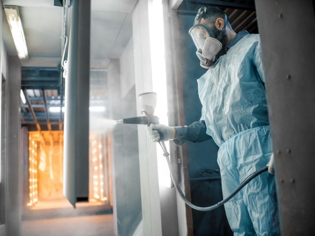 Metal technician powder coating metal sheet wearing protective equipment